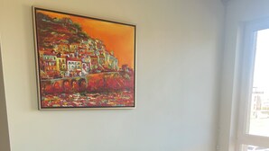 A room with a grey sofa, a painting of a colorful landscape, and a window with a view of the outside. - Two-room apartment 350 m from the beach, good infrastructure, quiet location (Sweti Wlas)
