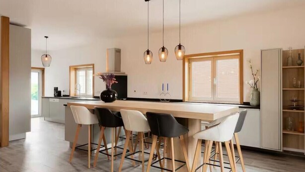 Una cocina moderna con una isla central, taburetes de bar, iluminación colgante y vistas al exterior.
