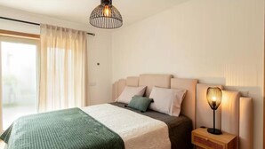 Un dormitorio con una cama, una lámpara de noche, una ventana con cortinas y una lámpara colgante.