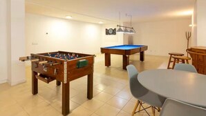 Una habitación con mesa de futbolín, mesa de billar y una mesa de comedor con sillas.