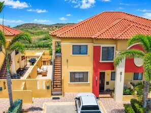 A residential building with a red-tiled roof, a staircase leading to a covered patio, and a parked car. - Gold Coast Oasis – Perfect 2BR/2BA for Your Island Stay (Noord)