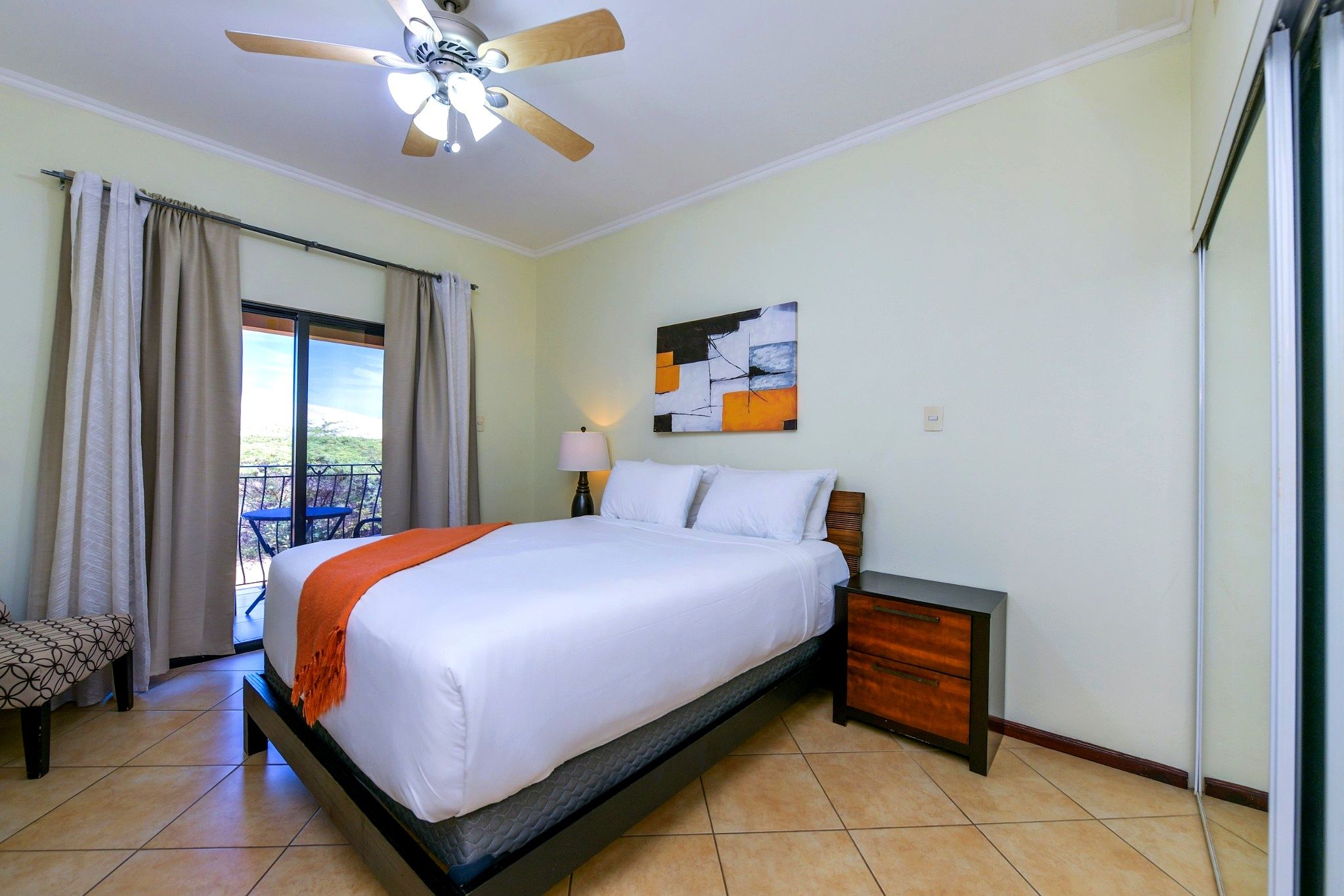 Une chambre d’hôtel comprenant un lit, une table de chevet, un ventilateur de plafond, une fenêtre avec des rideaux et une vue sur l’extérieur.
