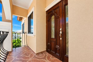 A corridor with a wooden door, a balcony with a metal railing, and a tiled floor. - Gold Coast Oasis – Perfect 2BR/2BA for Your Island Stay (Noord)