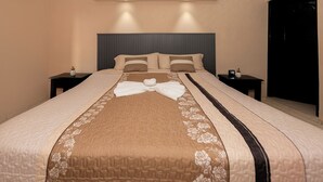 Un lit bien fait, recouvert d’une couvre-lit à motifs floraux et agrémenté d’un nœud, deux tables de chevet avec des réveils, et une tête de lit sombre.