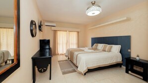 Une chambre d’hôtel comprenant un lit, des tables de chevet, un bureau, un miroir, un appareil de climatisation et un luminaire au plafond.