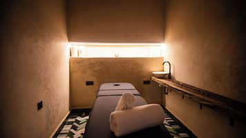 A small, dimly lit room with a single bed, a small sink, and a patterned floor.