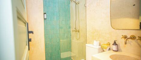 Un baño con cabina de ducha de vidrio, inodoro, lavamanos y espejo.