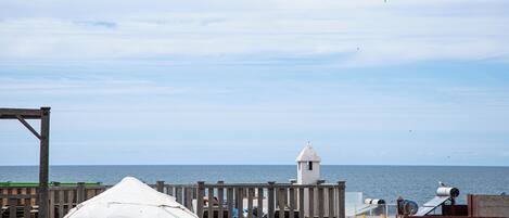 A coastal view with a wooden pier, a white building with a tower, and a white tent-like structure.