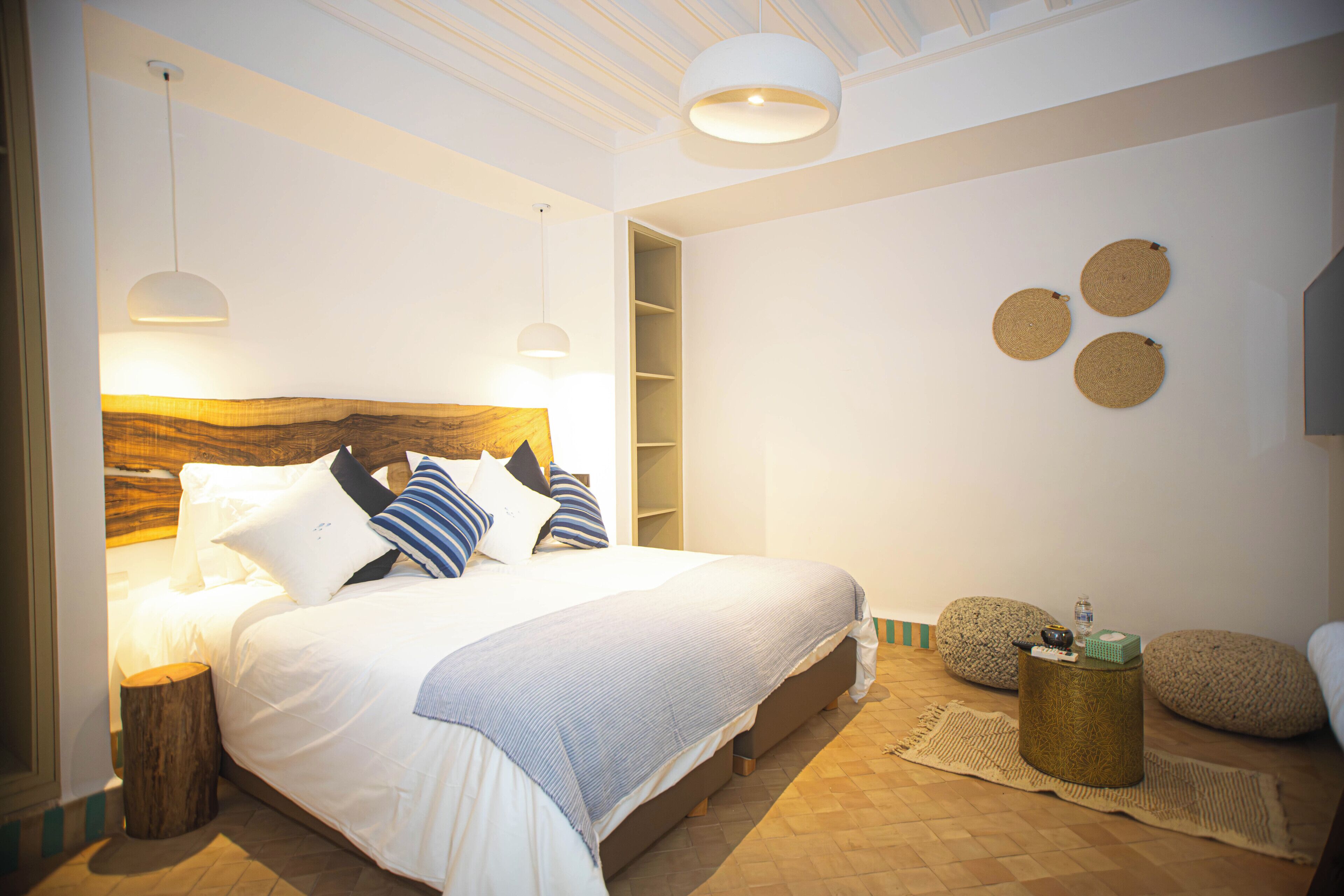 Ein Schlafzimmer mit einem großen Bett, Nachttischlampen, einem hölzernen Kopfteil, einem kleinen runden Tisch und einem an der Wand befestigten Regal.
