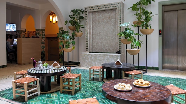 A lobby with a round dining table, several chairs, a reception desk, and potted plants.