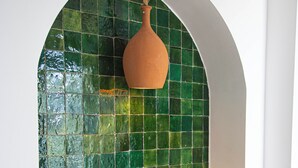 A room with a green mosaic wall, a woven basket, and a bench.
