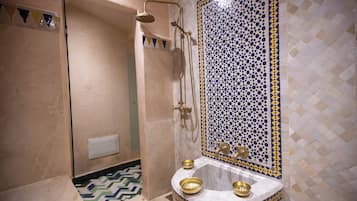 Une salle de bain avec une douche, un lavabo avec des cuves dorées et un mur recouvert de carreaux à motifs.