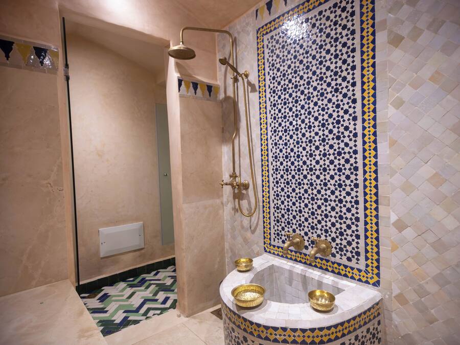 Une salle de bain avec une douche, un lavabo avec des cuves dorées et un mur recouvert de carreaux à motifs.