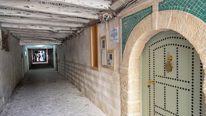 A corridor with a tiled floor, a door with a decorative pattern, and a sign on the wall.