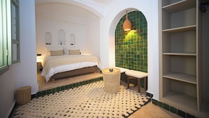 A bedroom with a bed, a small round table, a bench, and a green-tiled wall.