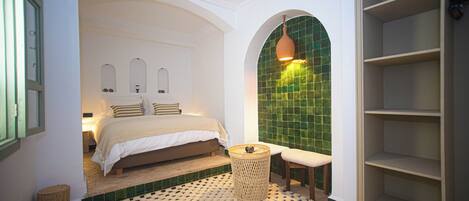 A bedroom with a bed, a small round table, a bench, and a green-tiled wall.