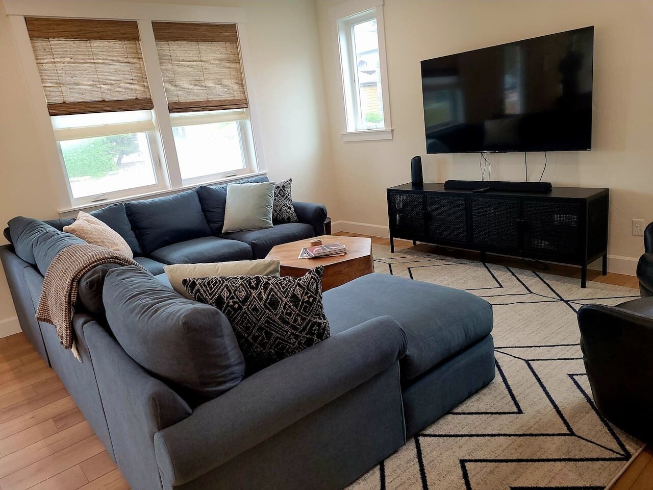 A modern living room with a sectional sofa, a coffee table, a flat-screen TV, and a black entertainment unit.