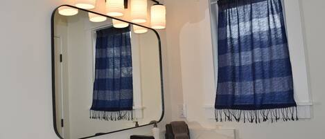 A bathroom with a large mirror, a sink, a towel, and a window with a blue curtain.