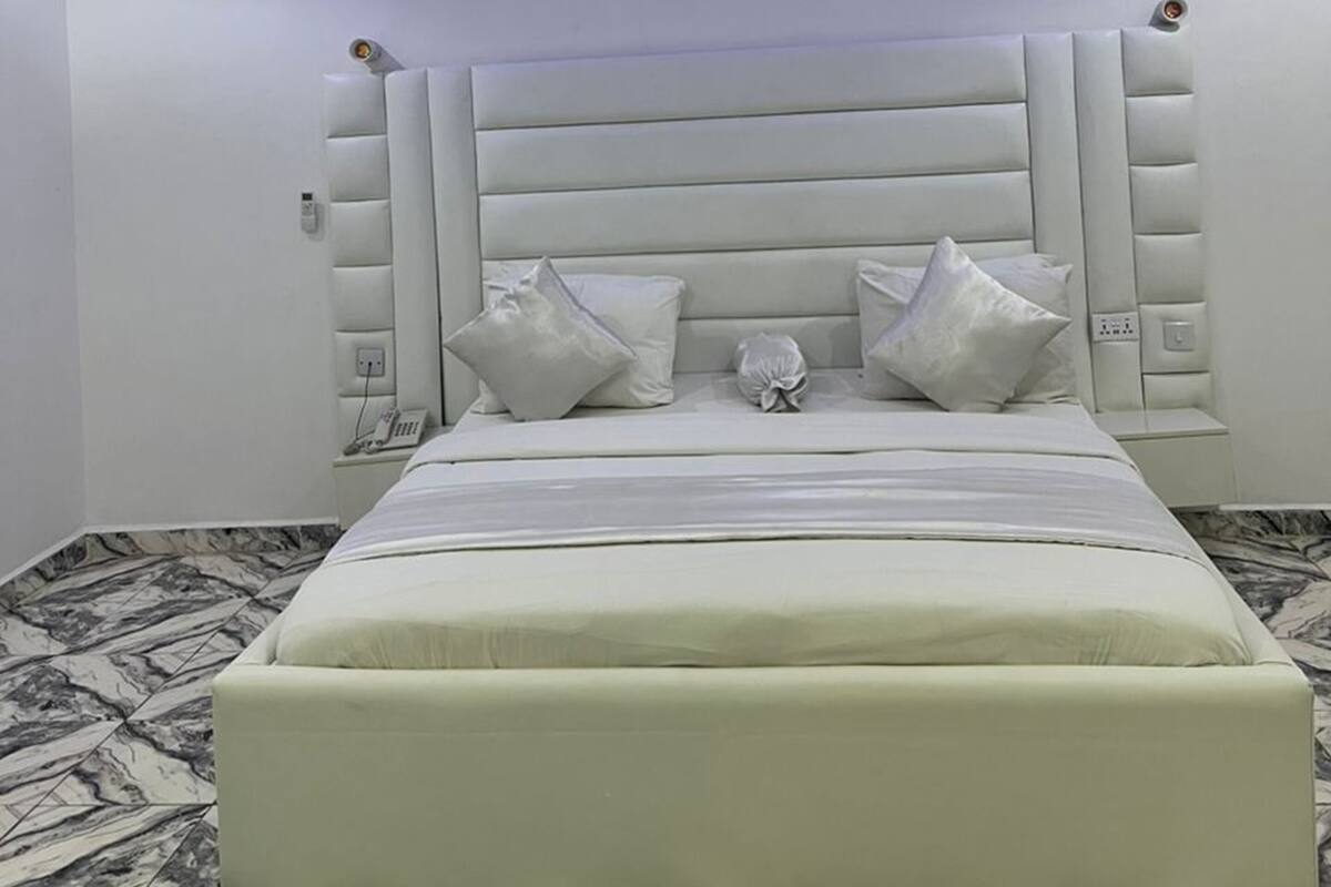 Une chambre à coucher moderne avec un grand lit, une tête de lit rembourrée et un sol à motifs de marbre.