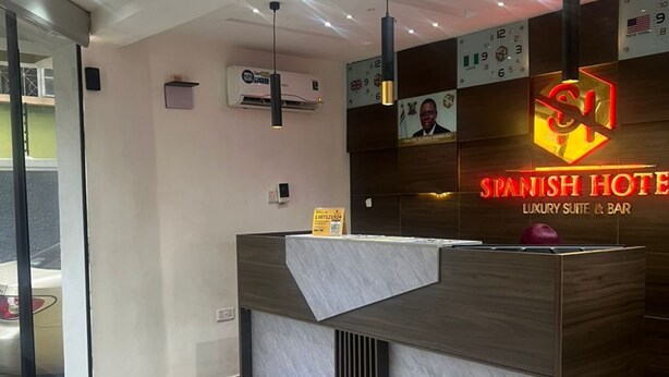 A reception desk with a modern design, a digital clock, and a sign for the Spanish Hotel. - Spanish Hotel Ikeja (Lagos)