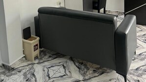 A modern room with a sofa, a TV mounted on the wall, a small table, and a window with blinds. - Spanish Hotel Ikeja (Lagos)