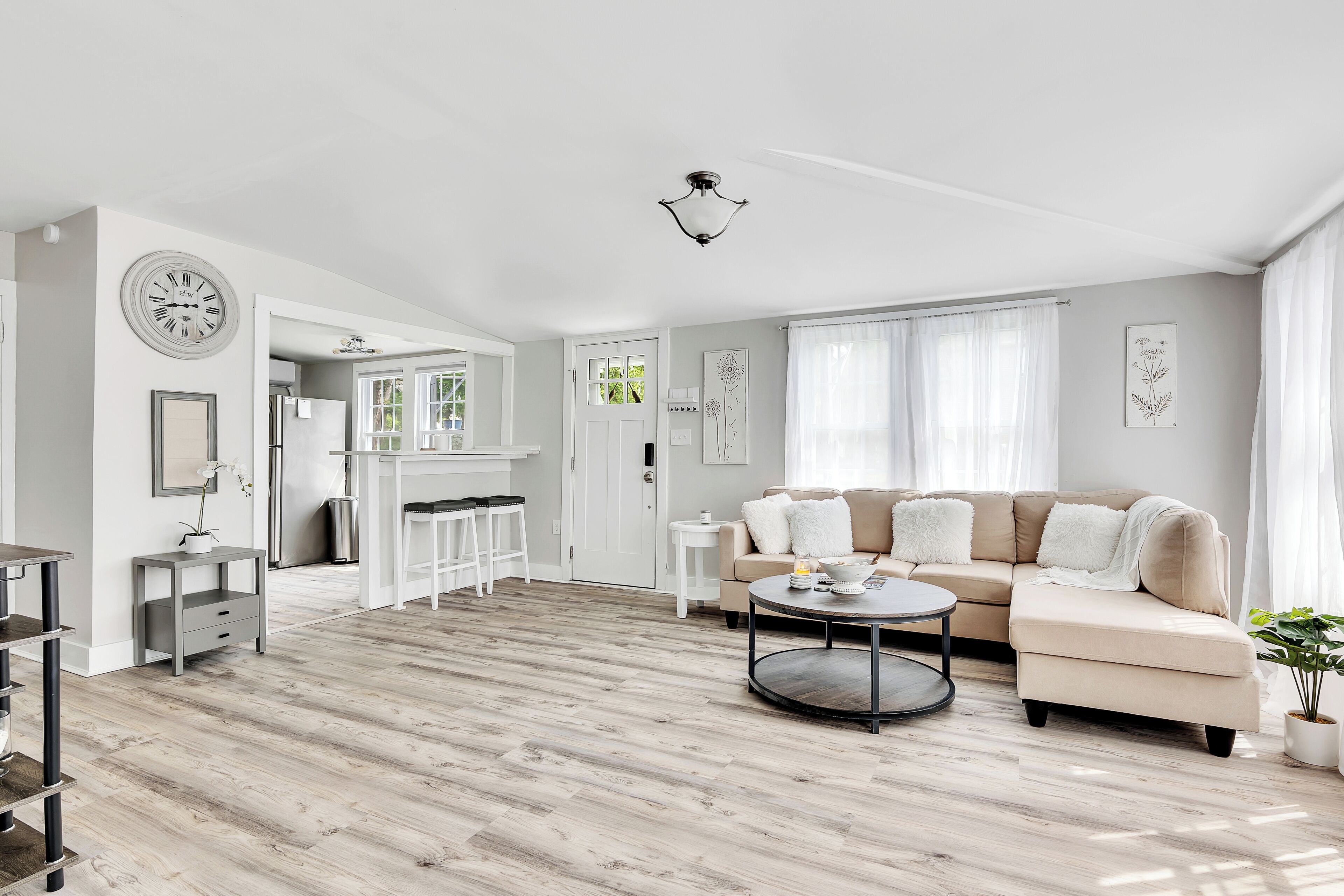 Ein modernes Wohnzimmer mit einem beigen Sofa, einem runden Couchtisch und einem Essbereich mit einem weißen Kühlschrank und Barhocker.