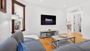 A modern living room with a flat-screen TV, grey sofas, a wooden floor, and a staircase in the background. - The Milton Manor 5BR 2BA - Sleeps 10 - Unit 2 (Milton)