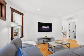 A modern living room with a flat-screen TV, grey sofas, a wooden floor, and a staircase in the background. - The Milton Manor 5BR 2BA - Sleeps 10 - Unit 2 (Milton)