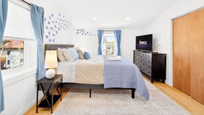 A bedroom with a bed, a TV, a dresser, and a window with curtains. - The Milton Manor 5BR 2BA - Sleeps 10 - Unit 2 (Milton)