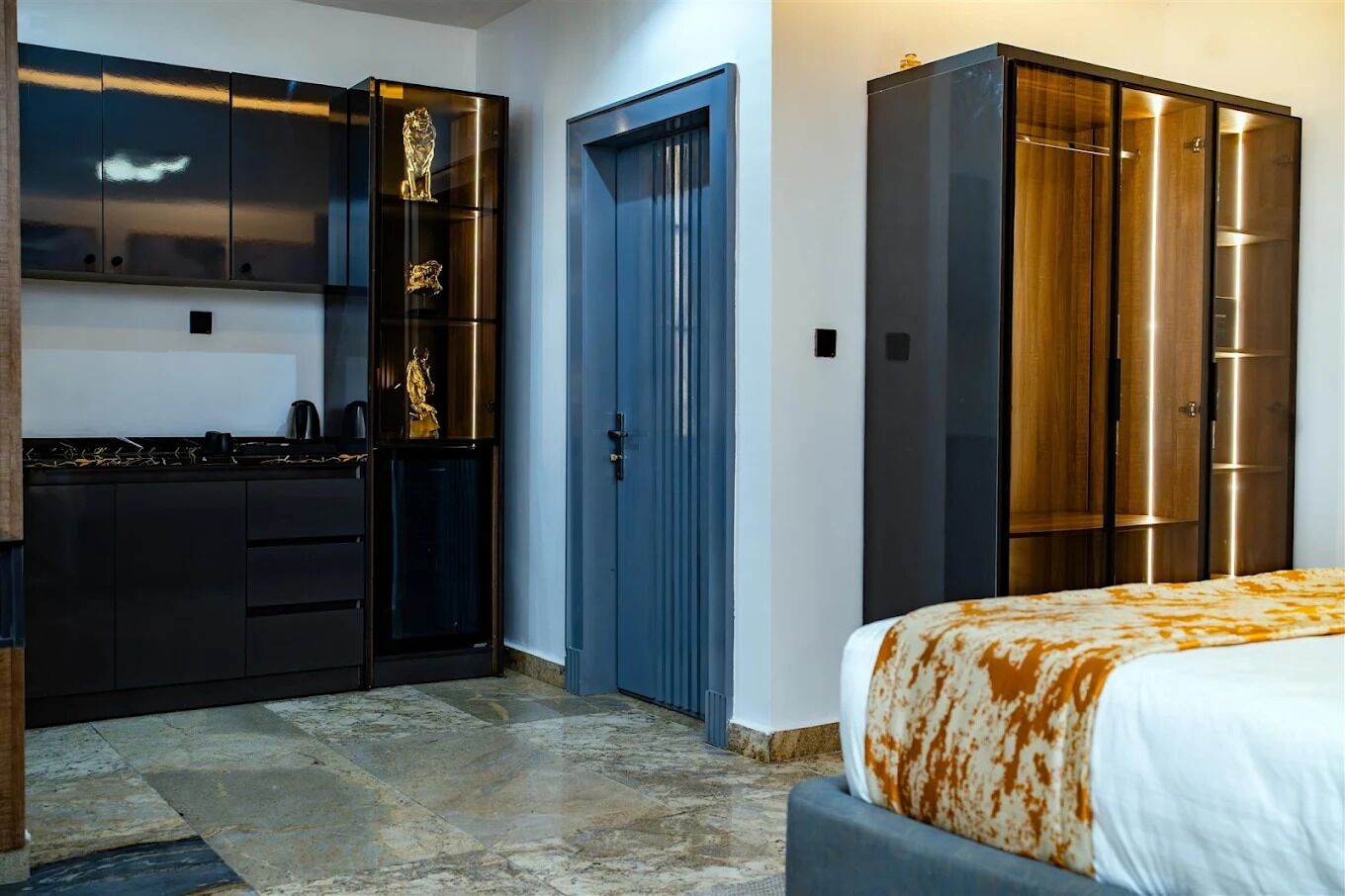 A modern bedroom with a bed, a wardrobe, and a built-in kitchenette.