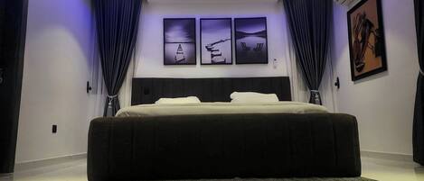 Une chambre à coucher moderne avec un grand lit, des spots encastrés au plafond et trois œuvres d’art encadrées accrochées au mur.