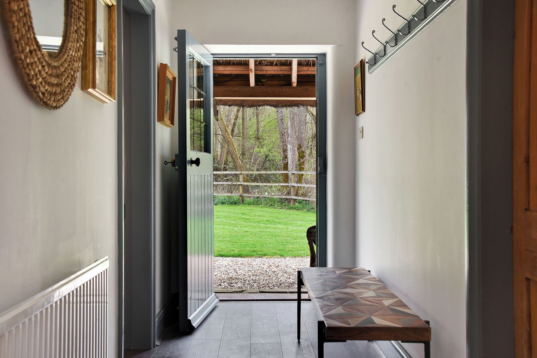 A hallway with a bench, a door leading to a grassy area, and a coat rack.