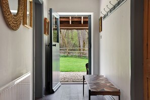 A hallway with a bench, a door leading to a grassy area, and a coat rack. - Home Farm Cottage (Peterborough)