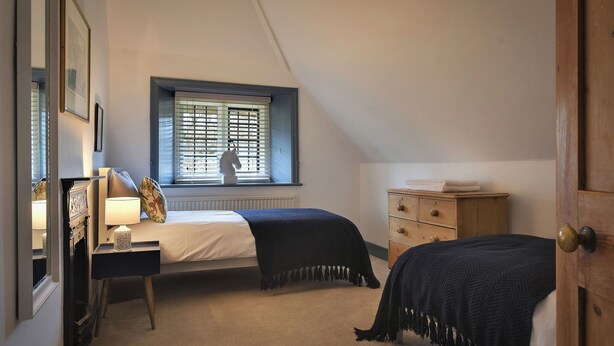 A bedroom with a bed, dresser, window with blinds, and a door. - Home Farm Cottage (Peterborough)