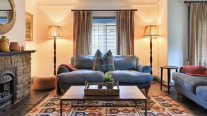 A cozy living room with a fireplace, two sofas, a coffee table, and patterned curtains. - Home Farm Cottage (Peterborough)