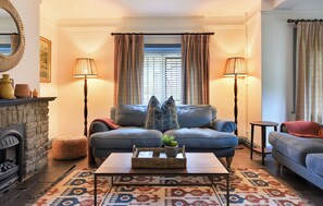 A cozy living room with a fireplace, two sofas, a coffee table, and patterned curtains. - Home Farm Cottage (Peterborough)