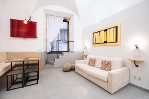 Un salon moderne avec un canapé, une petite table, un radiateur rouge, un escalier et une œuvre d’art accrochée au mur.