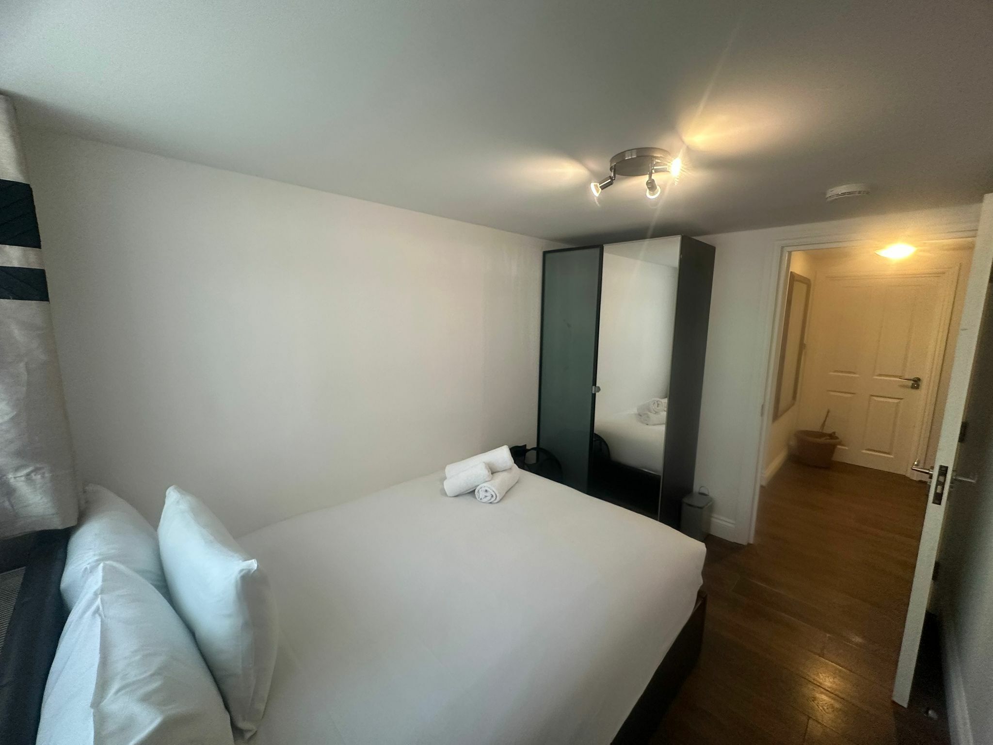 Une chambre d’hôtel avec un lit, des oreillers, un miroir, une porte et un couloir.