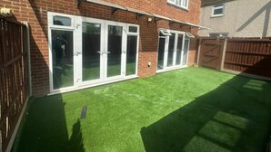 A residential property with a brick exterior, white-framed sliding doors, and a well-maintained artificial green lawn. - Modern 2 BDR APT Havelock Road UB2 (Greater London)