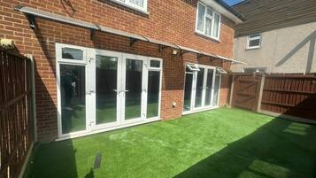 A residential property with a brick exterior, white-framed sliding doors, and a well-maintained artificial green lawn.