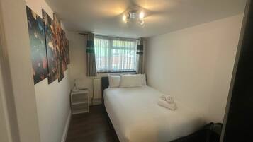 A compact hotel room with a single bed, a small bedside table, a radiator, and a window with curtains.