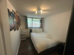 Ein kleines Hotelzimmer mit einem Einzelbett, einem Nachttisch, einem Heizkörper und einem Fenster mit Vorhängen.