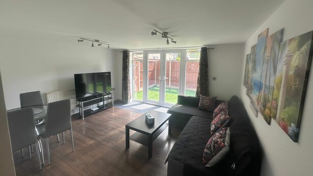 A living room with a flat-screen TV, a sofa, a coffee table, and a dining area with chairs. - Modern 2 BDR APT Havelock Road UB2 (Greater London)