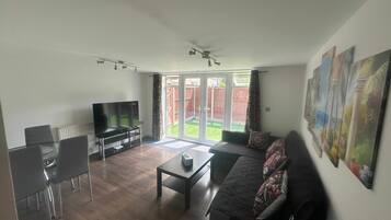 A living room with a flat-screen TV, a sofa, a coffee table, and a dining area with chairs.
