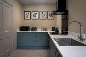 Una cocina compacta con gabinetes azul verdoso, un microondas, una cafetera y un lavabo.