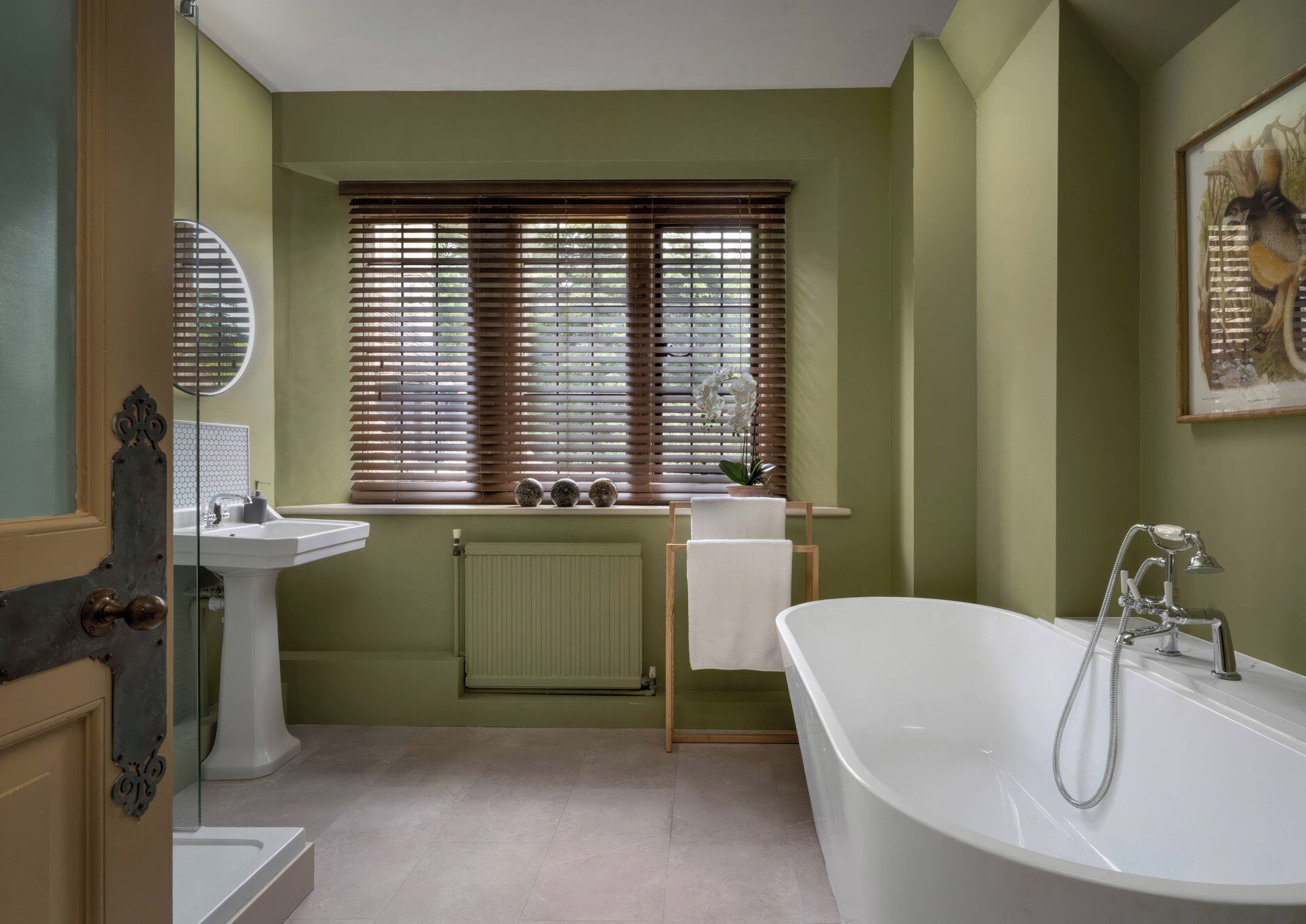 A bathroom with a bathtub, sink, window with blinds, radiator, and a framed picture on the wall.