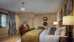 Un dormitorio con cama, cómoda, silla, lámpara y obras de arte en las paredes.