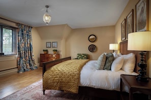 A bedroom with a bed, a dresser, a chair, a lamp, and artwork on the walls. - Rubens Rooms (Peterborough)