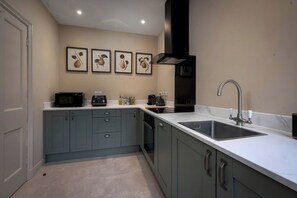 A modern kitchen with grey cabinets, a white countertop, a stainless steel sink, and framed artwork on the wall. - Rubens Rooms (Peterborough)