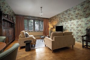 A living room with two sofas, a television, a wooden cabinet, and a patterned wallpaper. - Rubens Rooms (Peterborough)